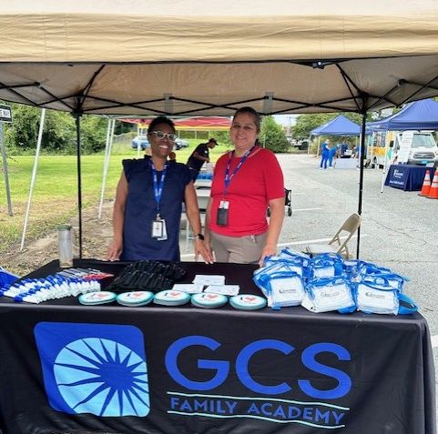 Two family academy members standing at a vendor table outside. 