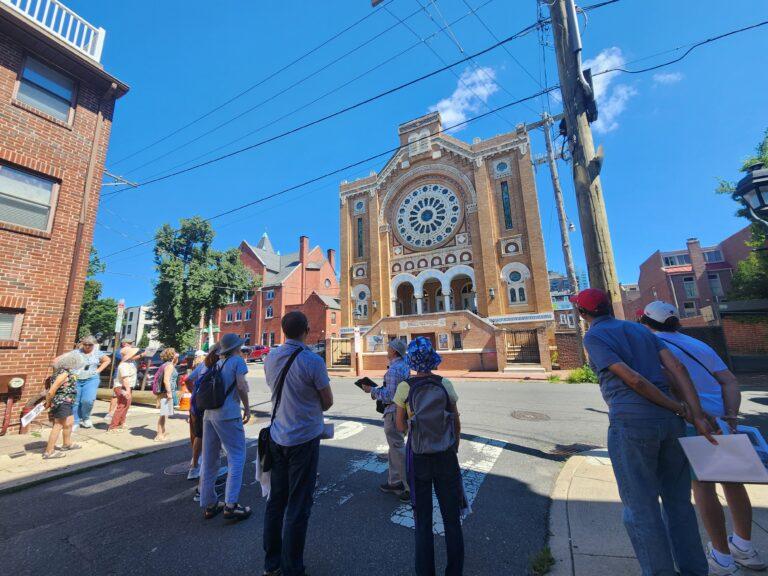Group of people walking as part of a tour, there's a colorful church in the background.