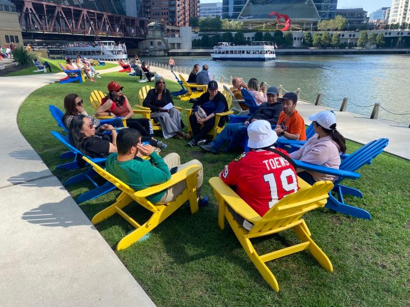 A group of people from PODER's team sit in colorful chairs along Chicago's Riverwalk