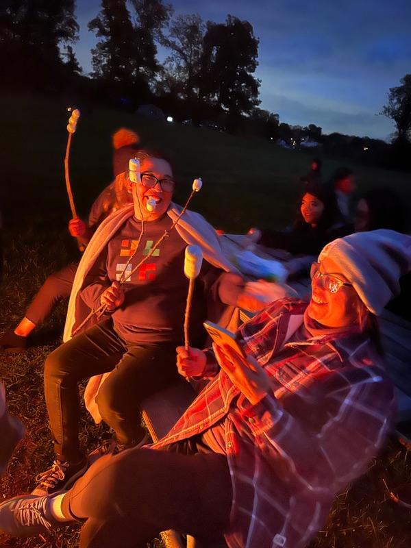 Griselda Piedra and another woman roast marshmallows over a campfire.