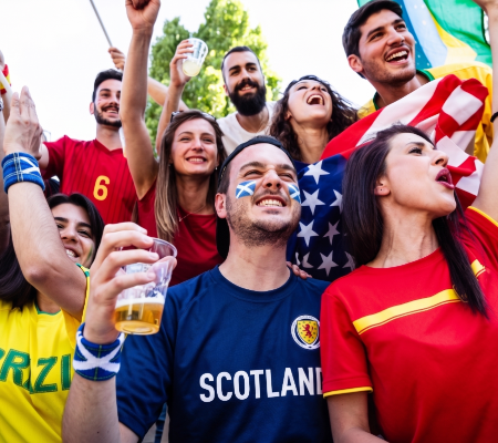 People cheering at sporting event with drinks, wearing country representation