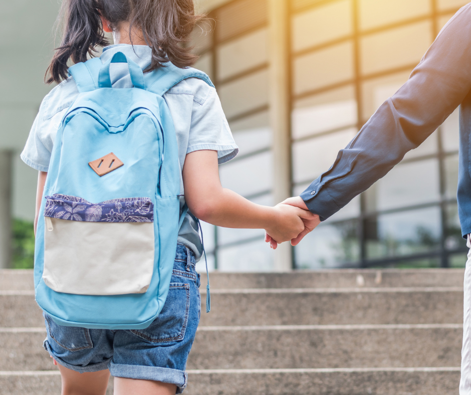 child holding parent hand entering school with backpack