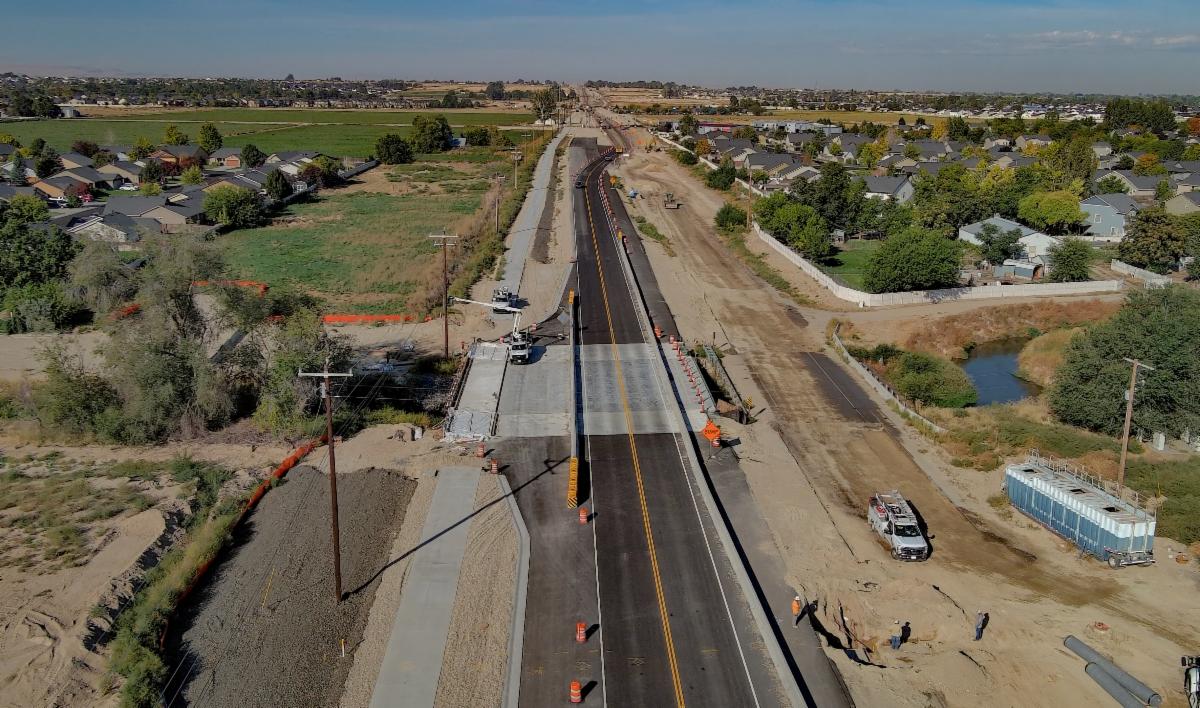 Aerial of the Wilson Drain Bridge crossing SH-55 with subdivisions and fields in the background under a blue sky.