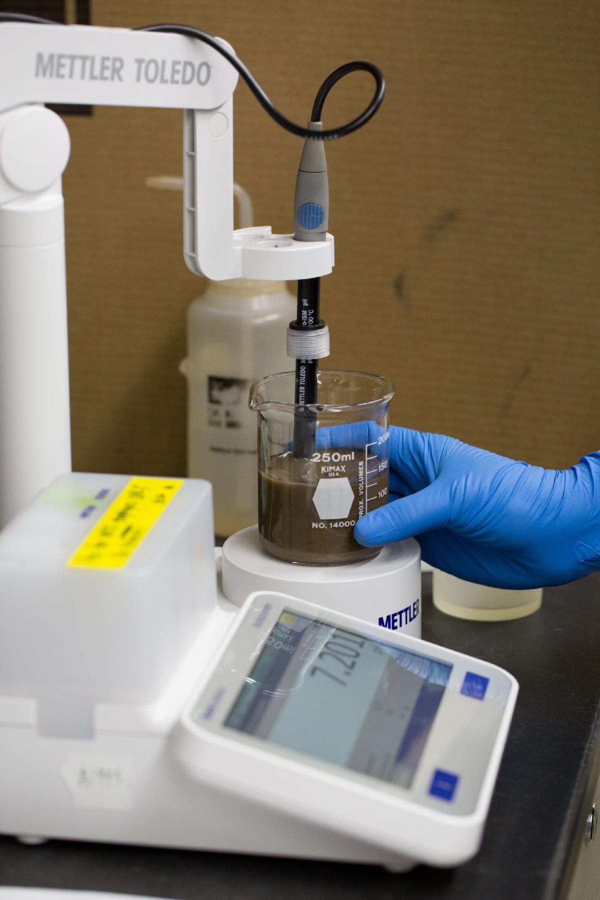 A piece of laboratory equipment measures Ph levels in a brown liquid in a beaker.