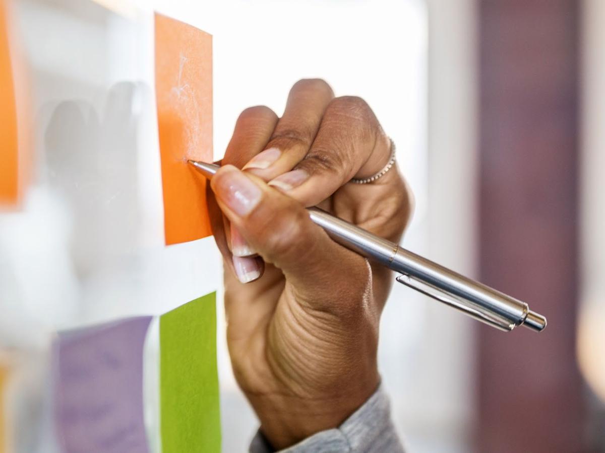 Hand writing on colorful sticky notes attached to a board.