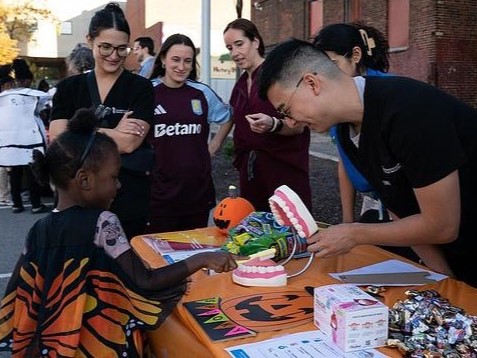 UMB volunteers engage with a child at Trick or Treat event, using a dental model to provide oral health education.