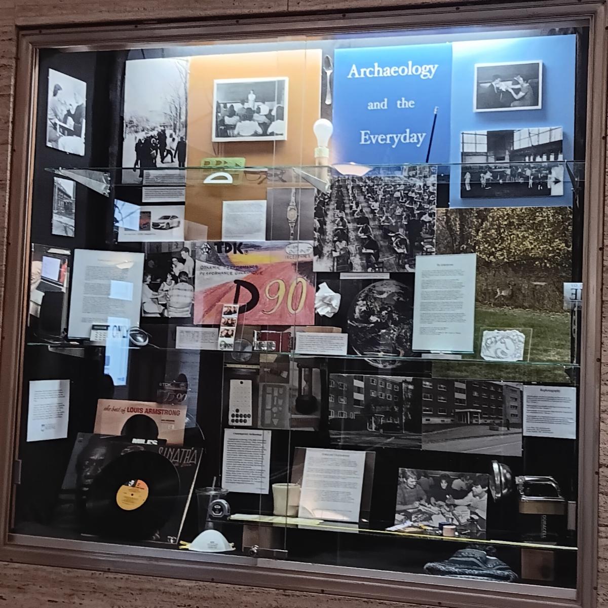 Photo of a large cabinet in which several texts, photographs and everyday items such as mugs and flashlights are displayed