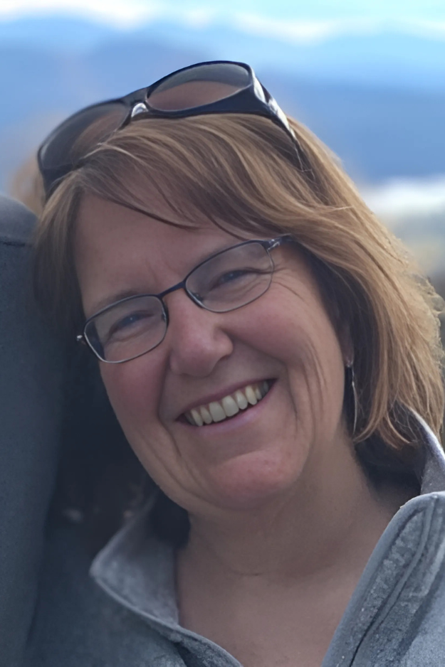 Photo of Betsy Rose, a smiling white woman with shoulder length brown hair.