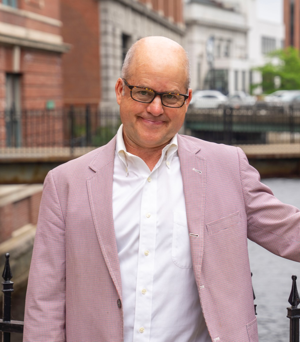 Photo of Professor Liam Riordan, a white man in a while shirt wearing a dusky pink jacket.