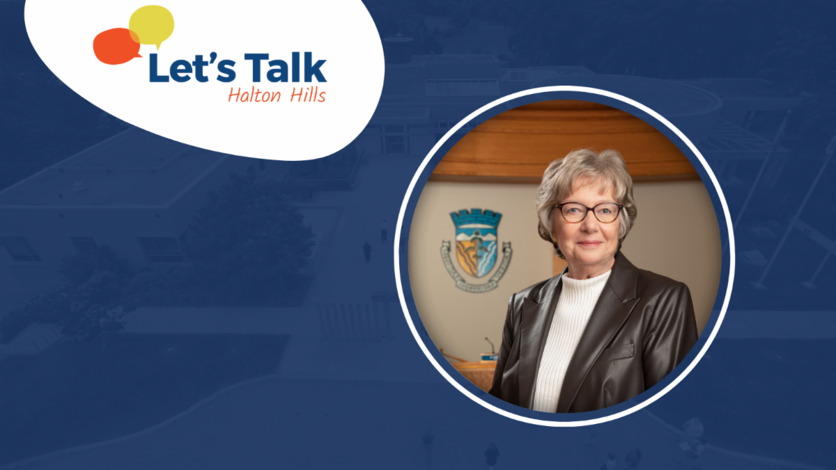 Logo with speech bubbles and text Lets Talk Halton Hills on a blue background circle frame showing the mayor of Halton Hills wearing a dark leather jacket and white top standing in front of a wall with a crest featuring blue and gold colours
