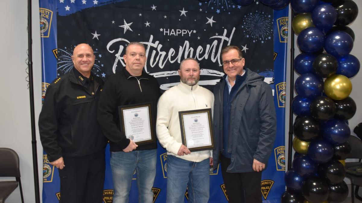 From left to right, Police Chief Paul Strong, Sergeant Paul Durant, Officer Matt Cunningham, and Mayor Robert Van Campen stand together indoors beneath a black, blue, and gold balloon arch. Sergeant Durant and Officer Cunningham hold framed citations, with a backdrop behind them that reads “Happy Retirement” and features Everett Police logos and star graphics.