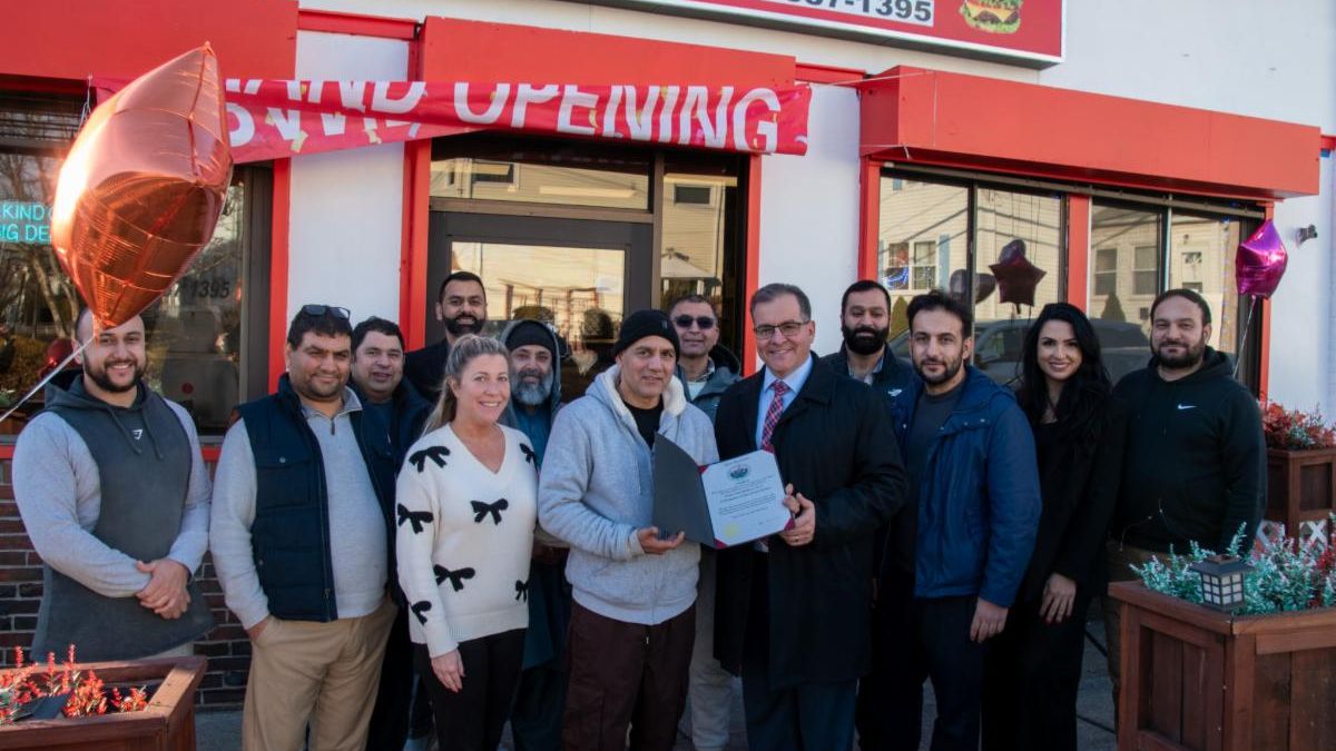Mayor Robert Van Campen presents a citation to the owners of Crown Fried Chicken and Pizza, alongside staff and City Councilors, in front of the restaurant.