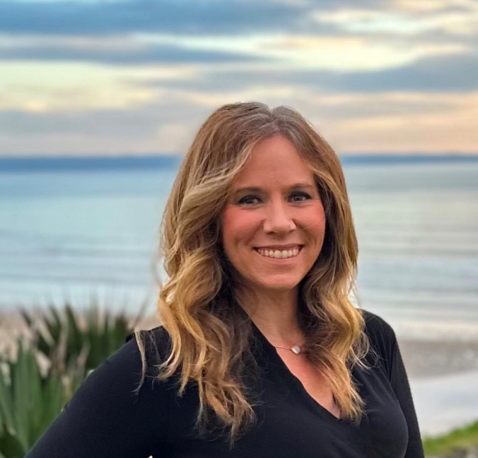 Sara Everett Brown, a confident woman with waves of blonde hair over her shoulders, moving with rhythm and motion. Dressed in a sleek black top, she stands polished and powerful, with a confident smile and steady presence. 
