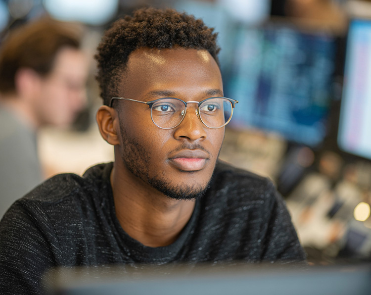 a young man at work wearing glasses, looking into a computer monitor