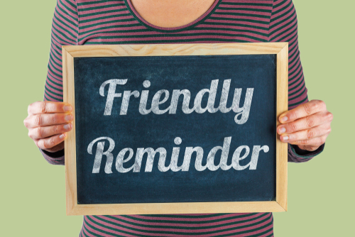 Female hands holding small black chalkboard in front of the body with written words saying Friendly Reminder