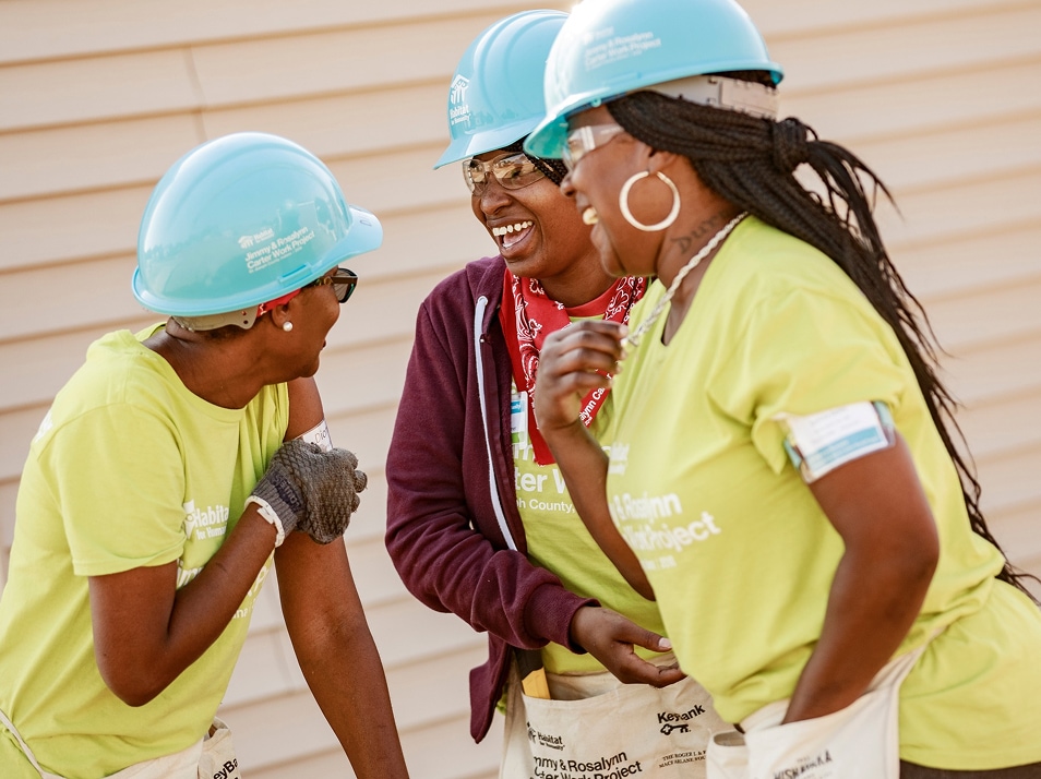 3 women in habitat hard hats engaged in lively conversation