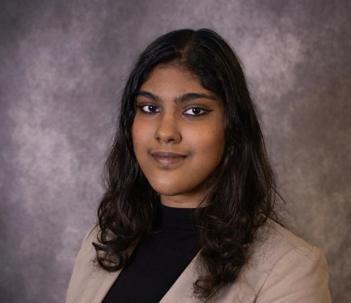 Headshot of young woman with dark hair wearing tan blazer and black shirt