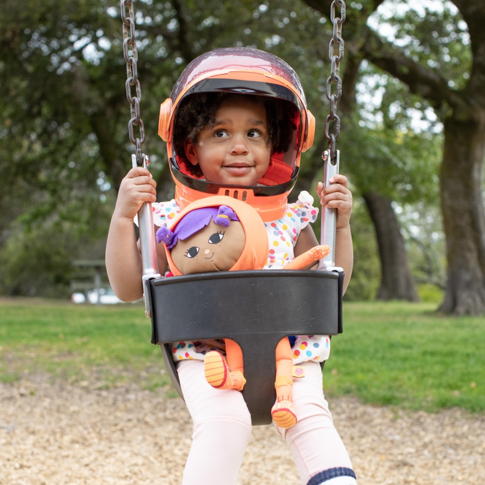 Young girl in swing wearing an astronaut costume holding an astronaut doll