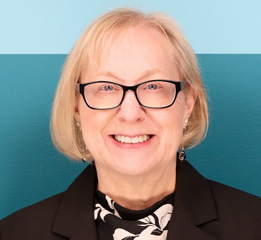 Karen Peterson woman with  blonde bob and glasseswearing black jacket and black and white shirt