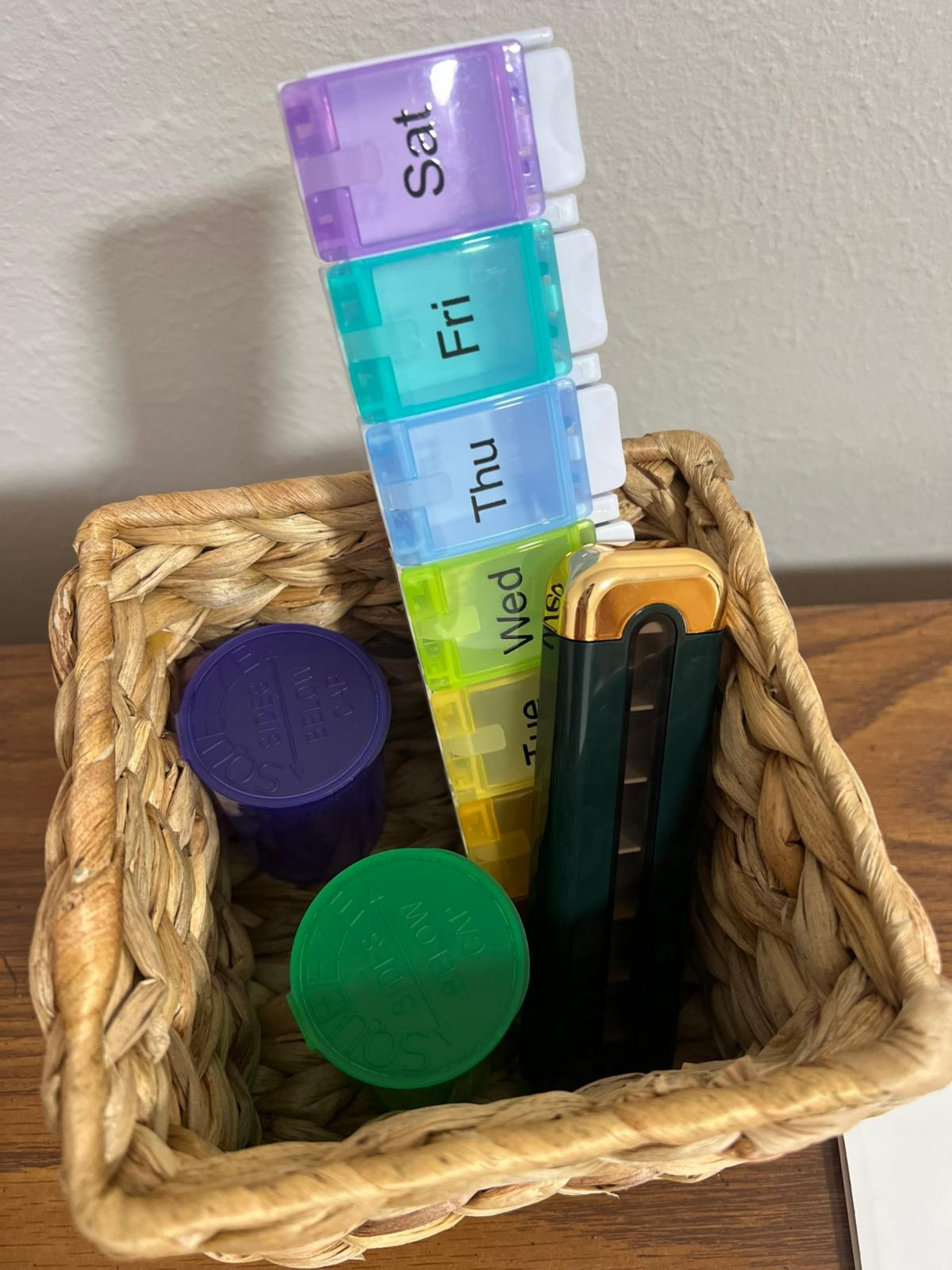 Weekly pill organizer and medication management supplies arranged in a basket to support medication independence and routine reminders