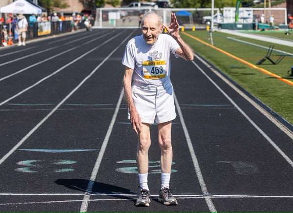 100 year old man poses on track smiling in shorts and tshirt