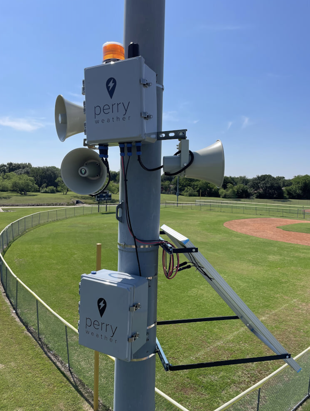 Perry weather siren equipment attached to pole next to park baseball field
