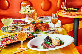 Colorful dining table and booth filled with various dishes and cocktails that have an orange hue
