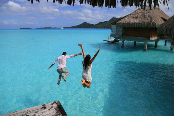 Couple jumping into crystal blue water in tropics