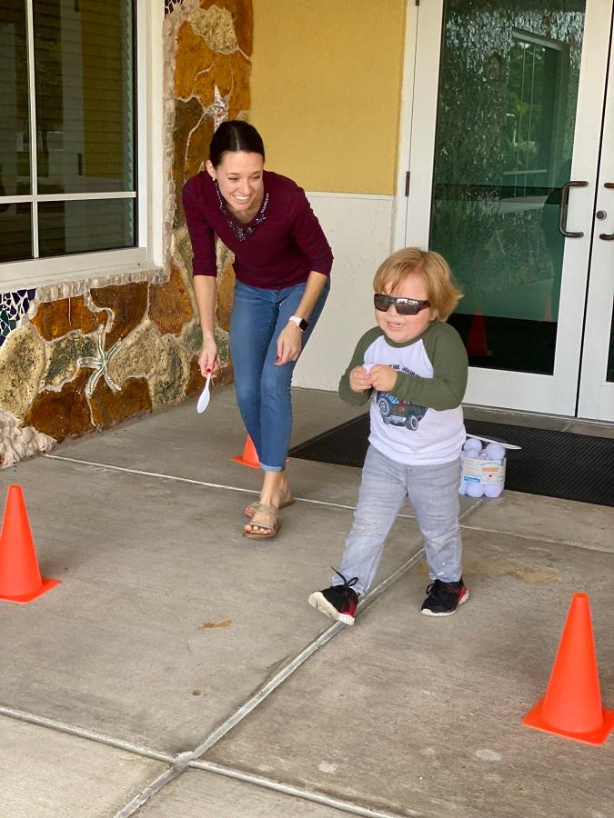 Teacher Tori Short helping a small boy run with snowball in a spoon