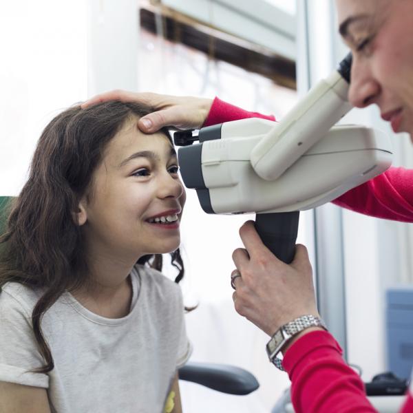Young girl with long brown hair getting vision checked by a doctor