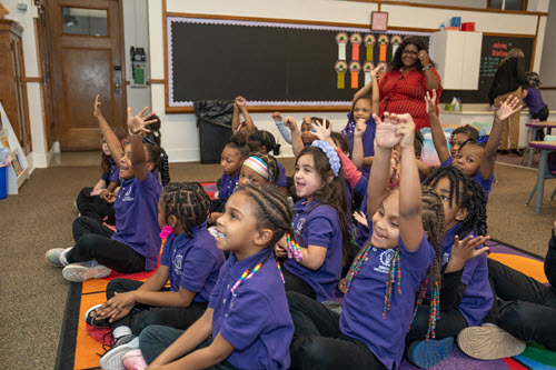 children sitting on the floor in a classroom with raised hands