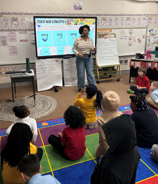 students in a classroom sitting on the floor looking at the teacher