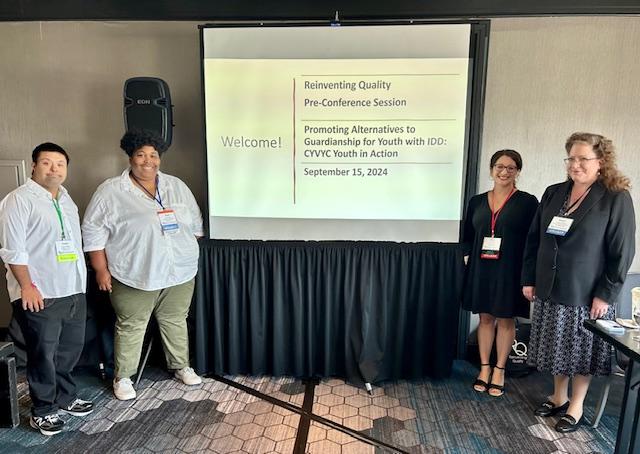 Four people stand by a screen