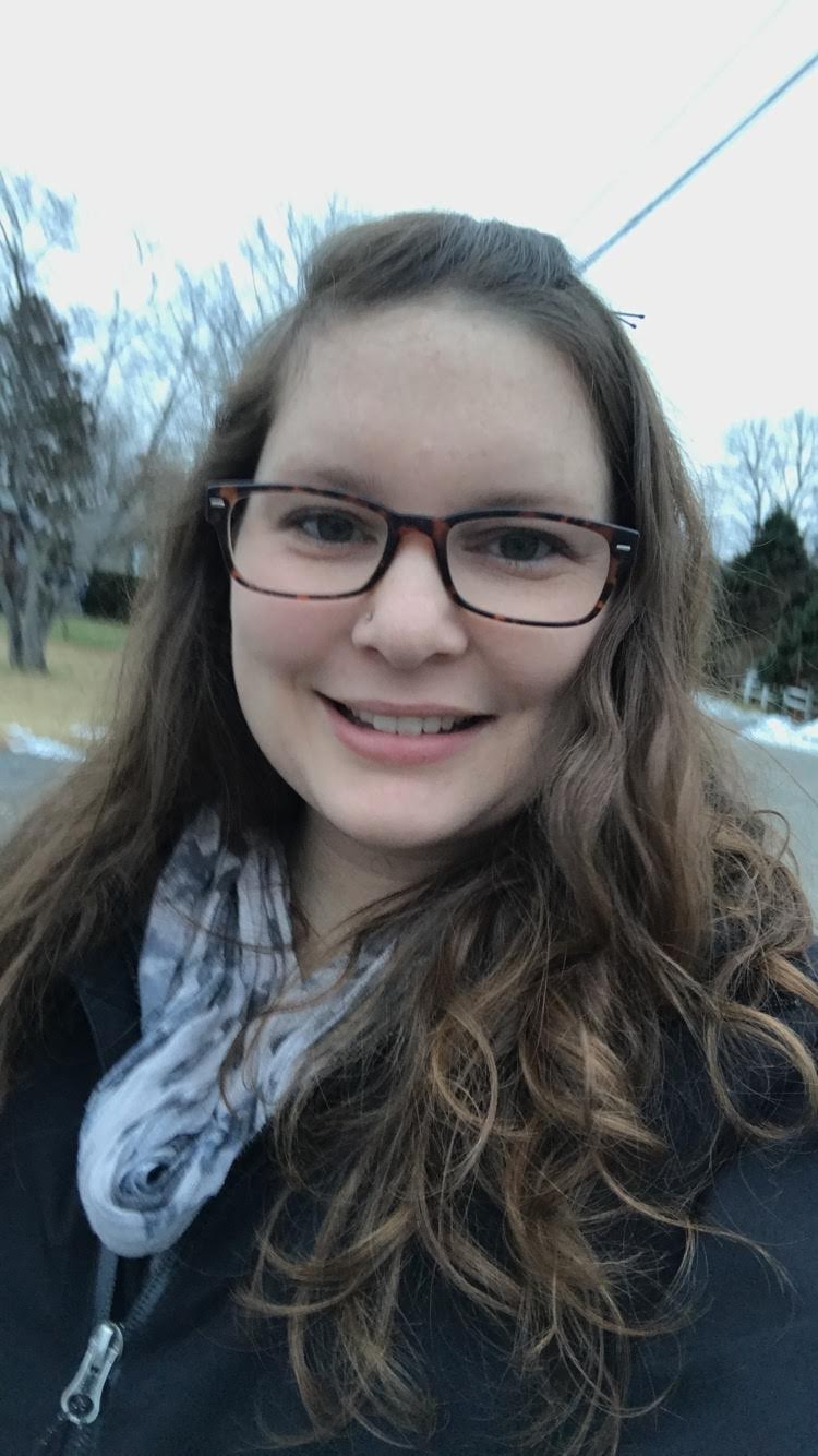 A young woman in glasses smiles at the camera