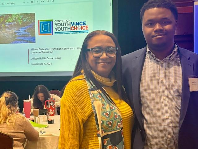 Two people take a photo in front of a screen