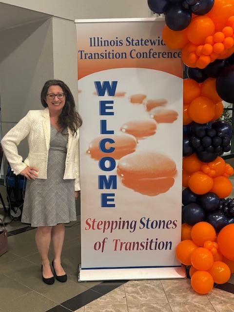 A woman stands with her hand on her hip by a sign