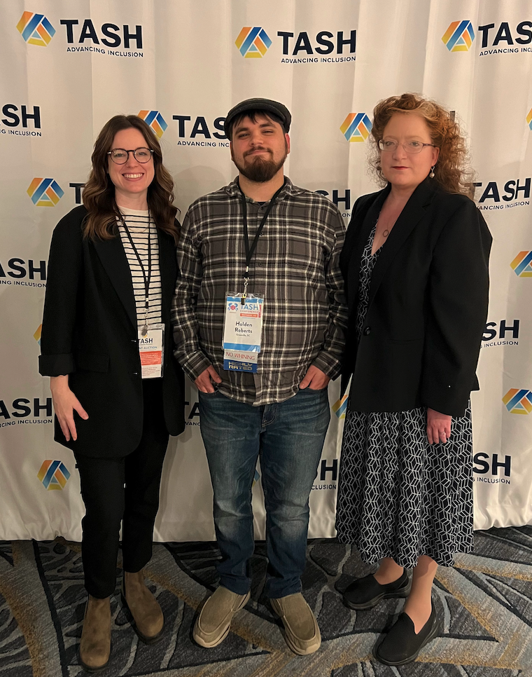 Three people stand in front of a TASH background
