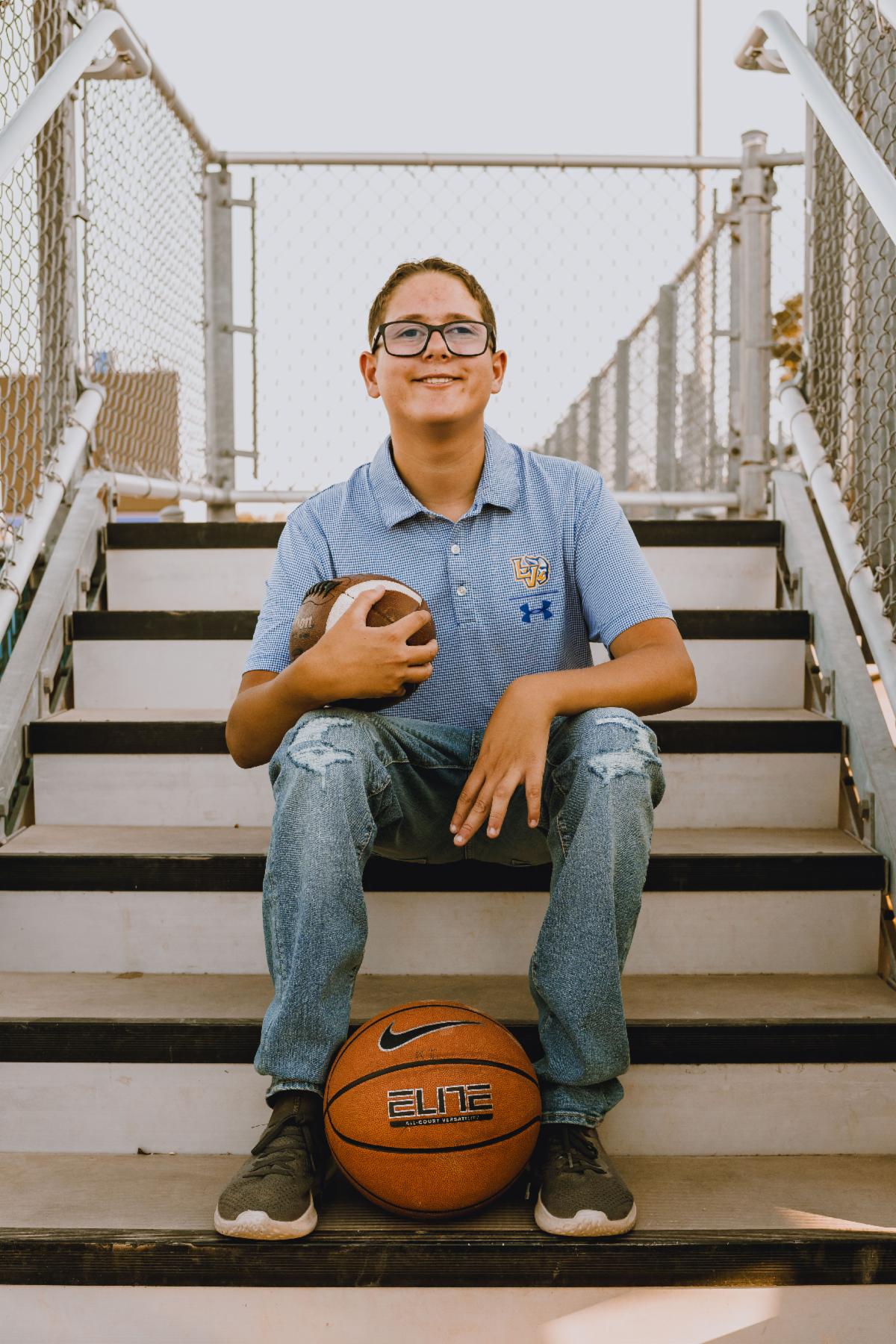 A young man in glasses sits on a step with a basketball between his feet