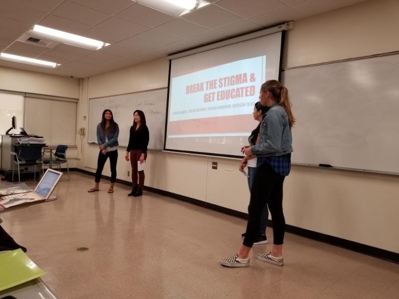 Four students giving presentation in a classroom. Students refer to powerpoint during presentation 