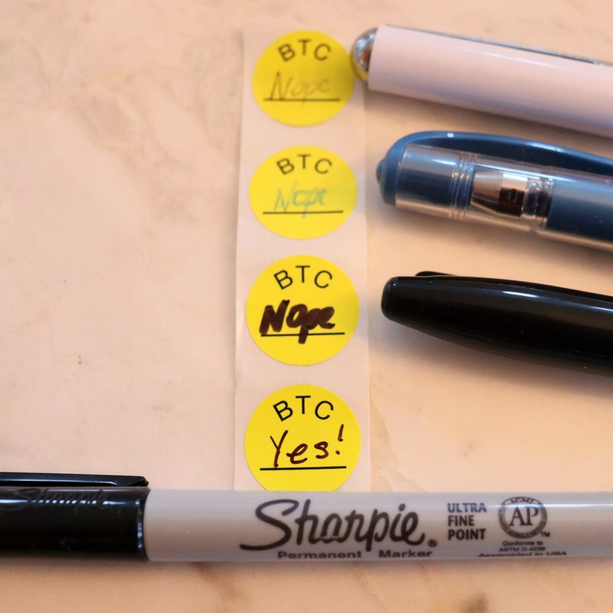 different pens shown with writing on BTC stickers showing a sharpie at the bottom with clear writing
