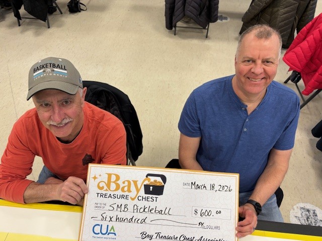 man in orange top and ball hat with man in blue shirt holding oversized honorarium cheque