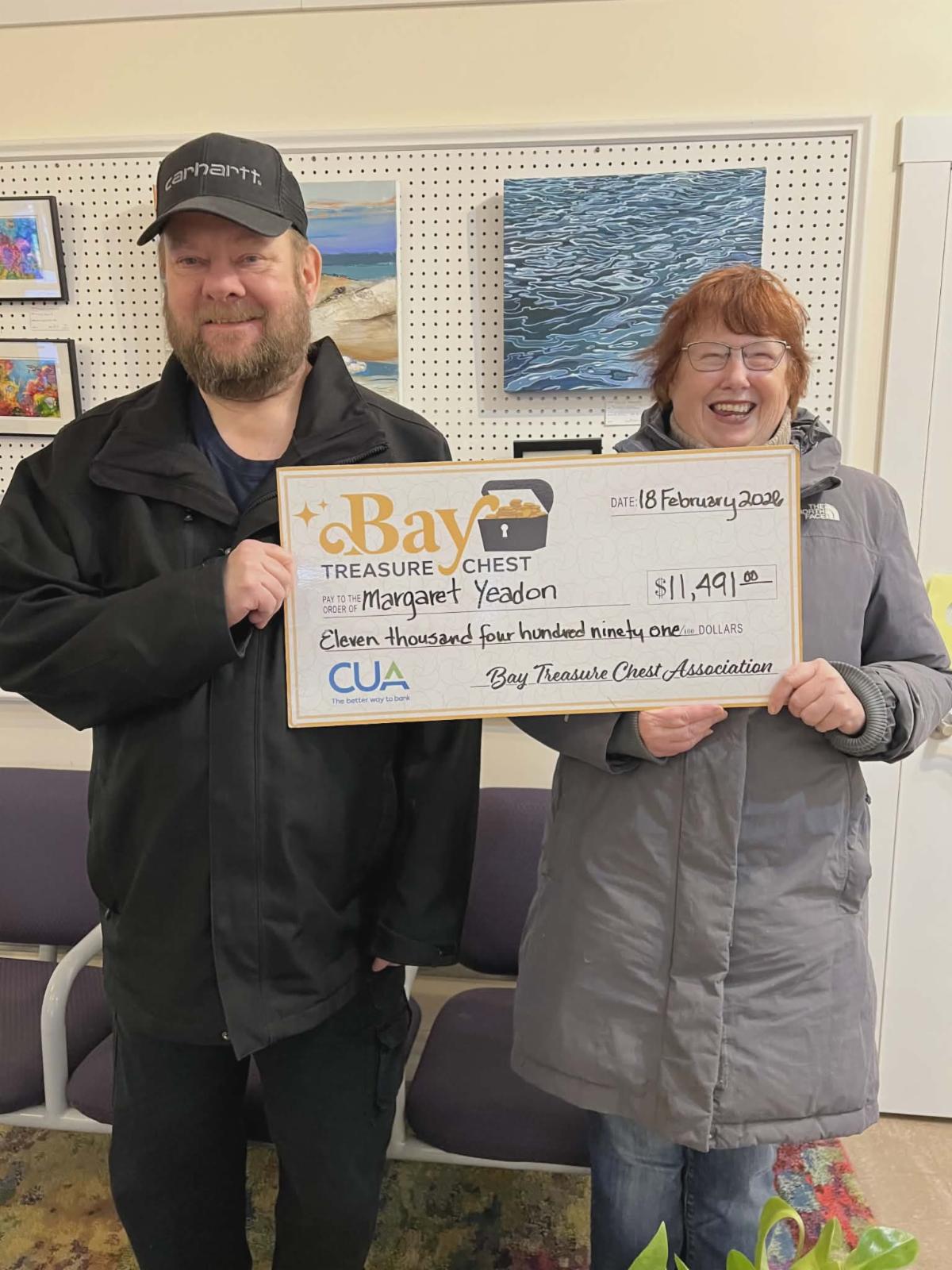 BTC winners holding a large oversized cheque showing a man in a black jacket and a woman in long great coat