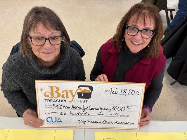 women in black turtleneck sweater, with a woman in a burgundy top holding a large honoraium cheque