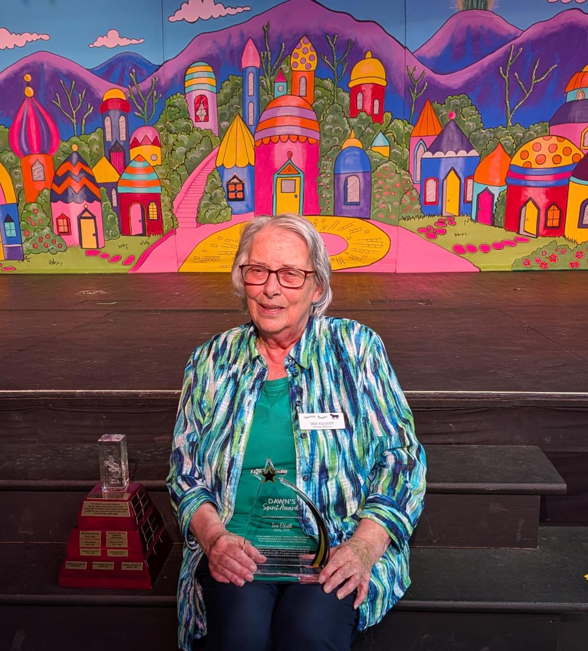 Unicorn Theatre artistic director sitting in front of a colourful mural holding an award