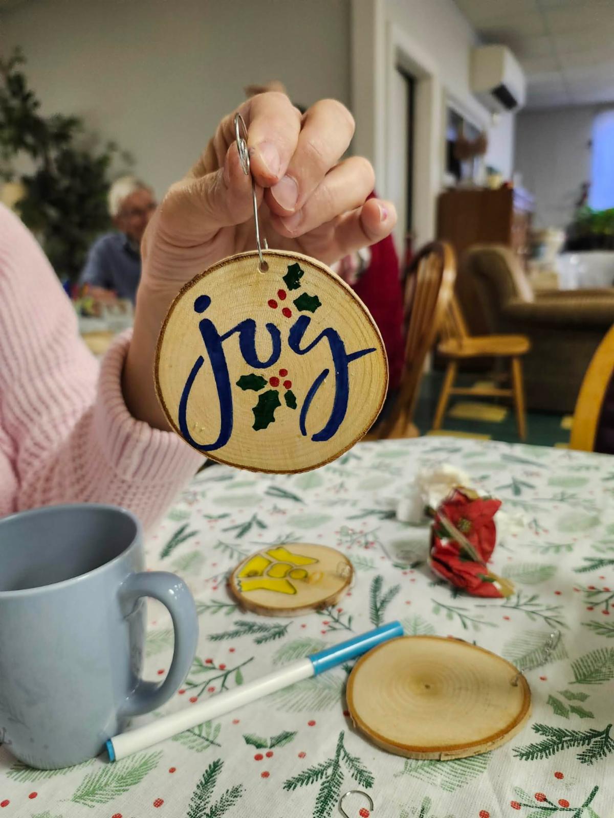 a persons hand holding a handmade raw edge wooden ornament saying the words joy