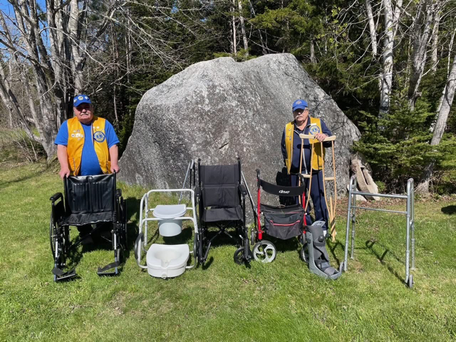 man on left  and right wearing blue shirts with Lions Club vest standing in front of a large rock outside with medical equipment available on loan