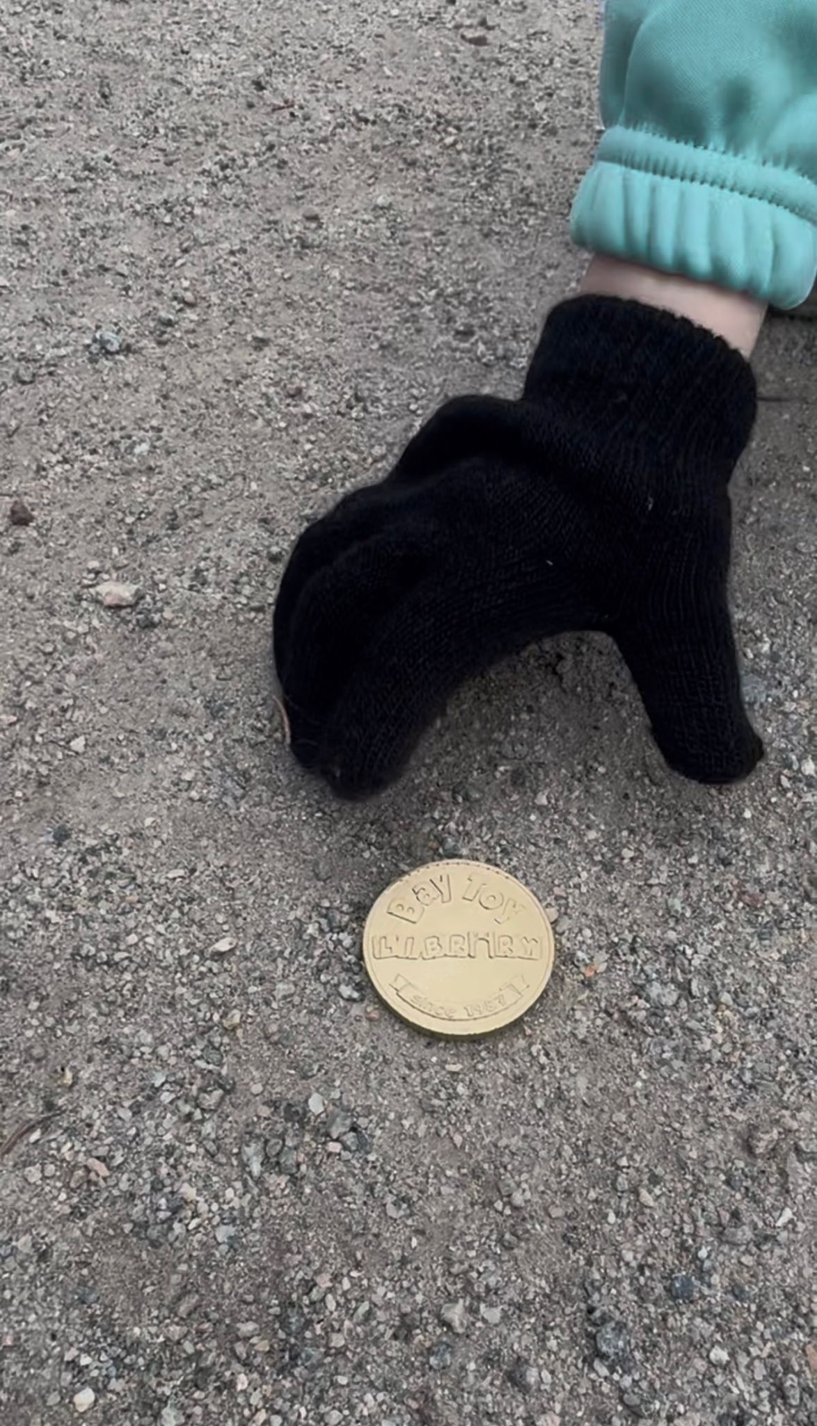 a hand in a black mitten picking up a handmade gold coin 