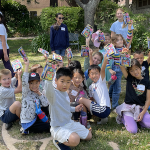 Outdoor photo of elementary-age kids at VBS all smiling and holding up their little art projects