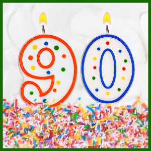 Birthday number candles 9 and 0 sitting in rainbow sprinkles on white frosting