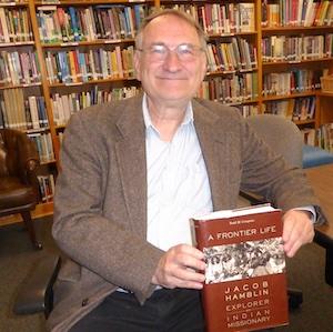 Todd Compton sitting in a library holding a book titled A Frontier Life